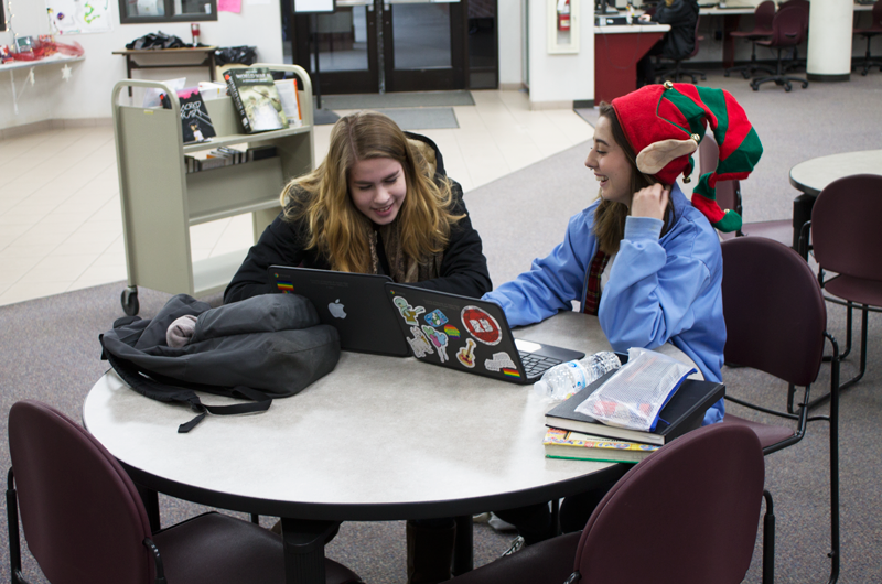 Seniors+Nicole+Fishman+and+Olivia+Herider%2C+in+a+festive+hat%2C+study+in+the+library.+Photo+by+Jacob+Thrasher