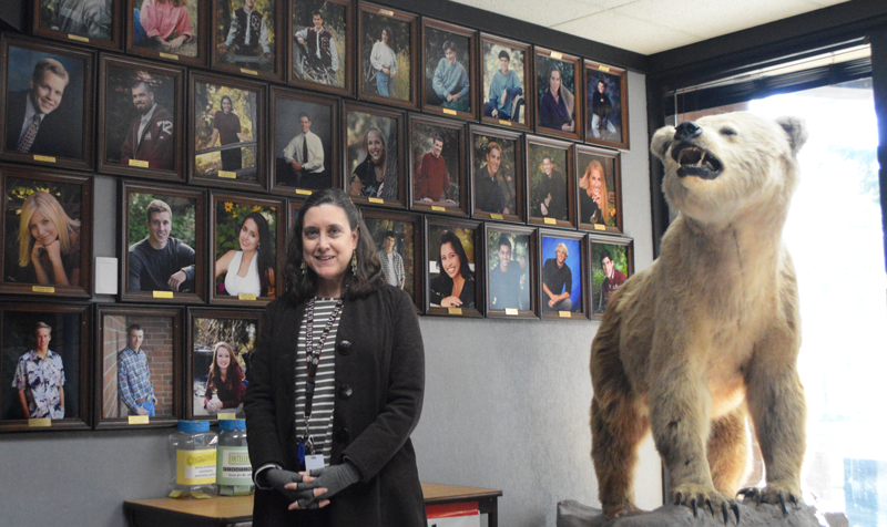 Counselor Cindy Henry-Grimm stands in front of the portraits of past ASB presidents. Photo by Taylor Wohlgemuth