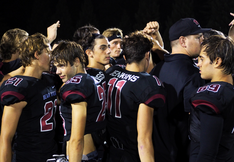 Varsity Football players huddle during a game. Photo by Kalei Owen